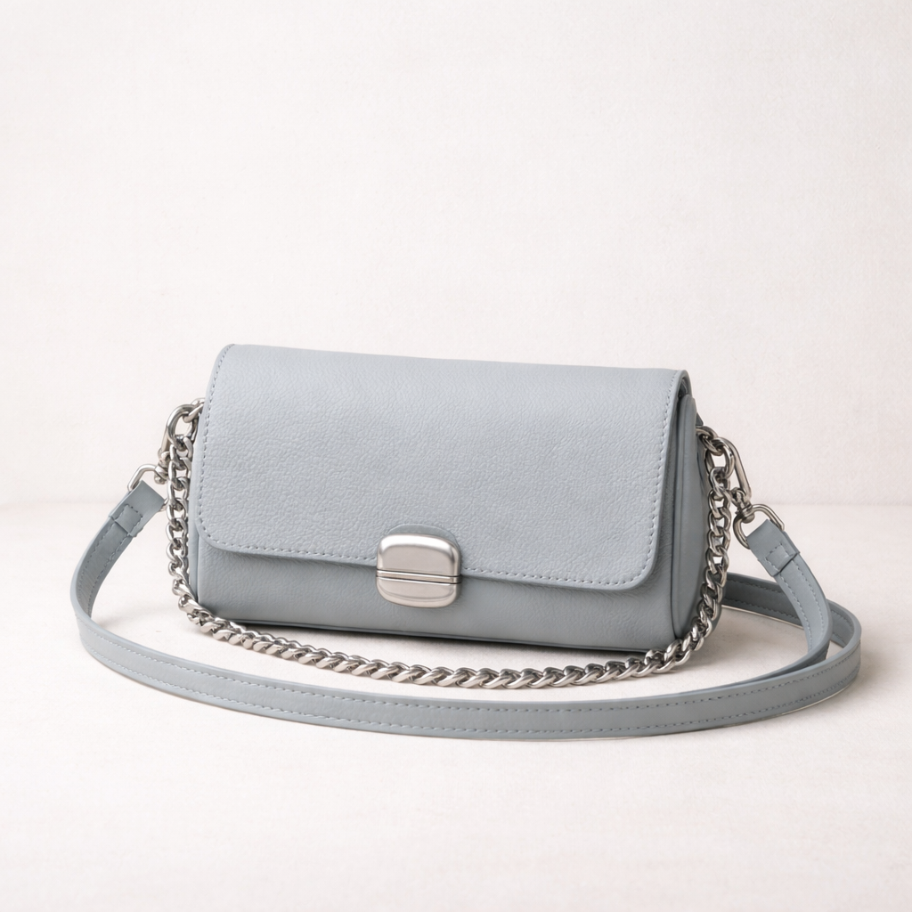 Light gray leather crossbody bag with silver chain strap on a clean off-white studio background
